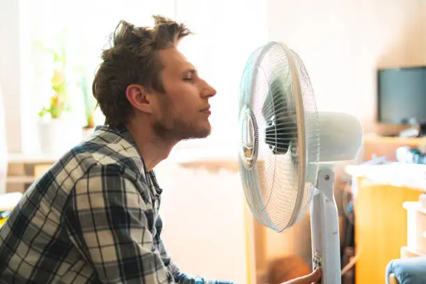 Photo of person enjoying the electric fan, cooling his face at home, during summer heat