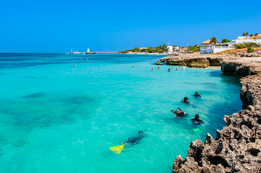 Tourists enjoying the turquoise clear waters at Malmok Beach in Aruba, where small bays interrupt the limestone coastline and make it a popular snorkeling spot.