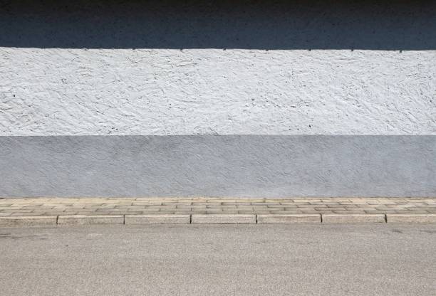 istock Wall painted with three horizontal stripes, one white, one black and one gray. Tiled sidewalk and an asphalt road in front. 1166212699