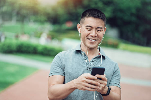 Asian ethnicity man texting in the park Portrait of a smiling middle aged man with a cell phone in the park masculinity photos stock pictures, royalty-free photos & images