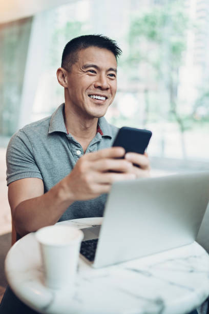 Smiling man with smart phone and laptop in cafe