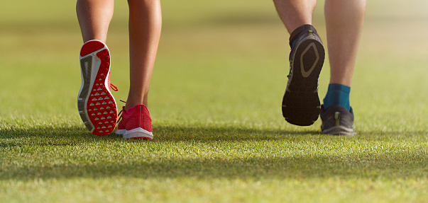 Couple runners athletes feet running on grass. Female y male fitness sunlight jogging workout. Sport athlete active lifestyle concept. Athletic pair of legs running on grass during sunset city park