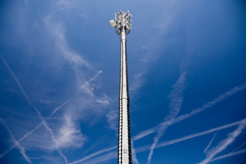 cellular radio antenna in front of an bright summer sky full of vapor trails caused by airplanes.