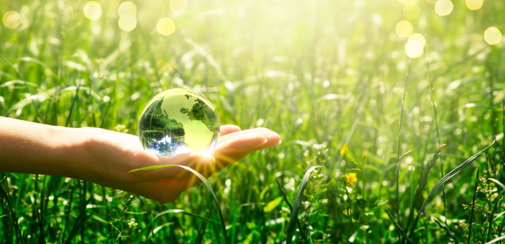 Earth crystal glass globe in human hand on grass background. Saving environment and clean green planet concept. Card for World Earth Day concept.
