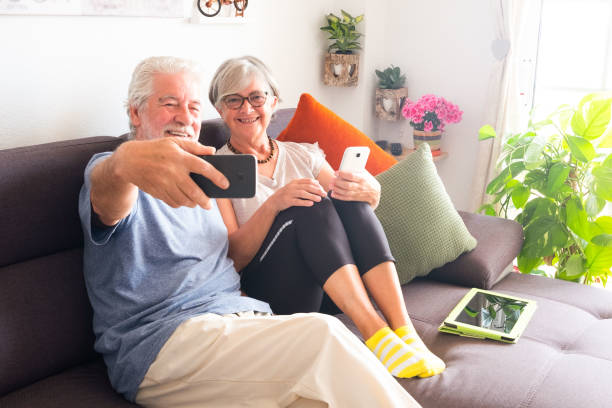 istock Two senior people take a selfie smiling and relaxing on the sofa. Bright light from window. Technology and wireless 1166246940