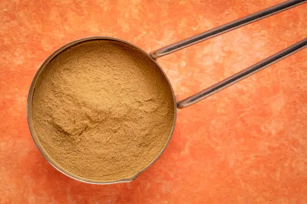 green coffee beans powder - metal measuring scoop against orange textured paper