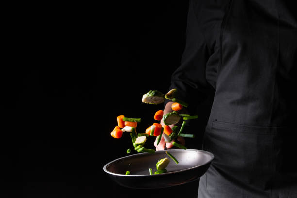 istock Chef preparing vegetables in a pan, Asian cuisine, on a black background for design, recipe book, menu, restaurant or hotel sign, cooking, gastronomy 1166250367