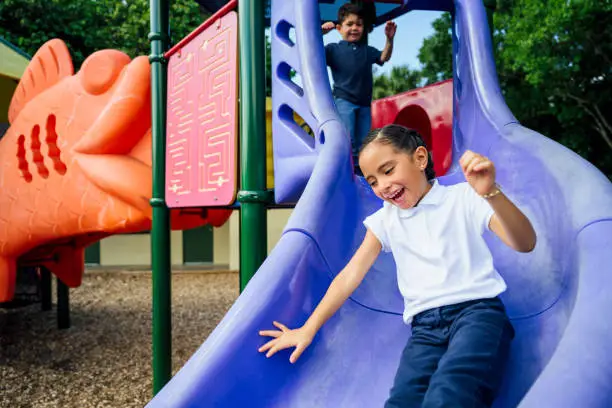 Photo of Hispanic schoolgirl sliding on playground equipment