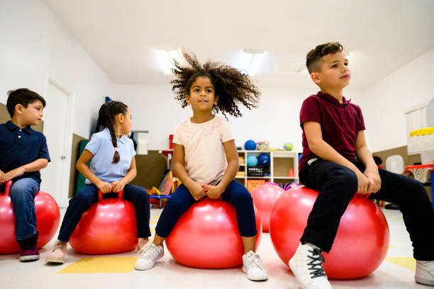 Hispanic elementary students exercising on fitness balls Group of elementary aged male and female Hispanic students bouncing on fitness balls in school playroom. fitness ball stock pictures, royalty-free photos & images