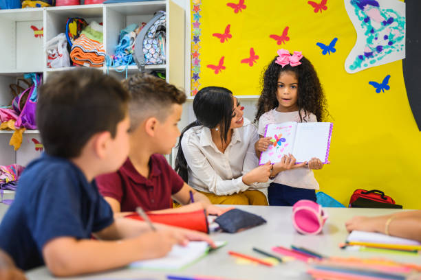 istock Hispanic schoolgirl showing drawing to classmates 1166252090