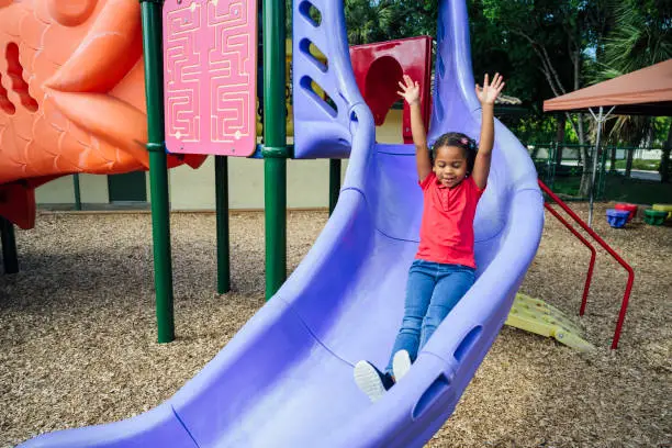 Photo of Hispanic schoolgirl enjoying sliding on playground equipment