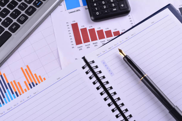 istock Blank Notebook with calculator, keyboard and fountain pen on graphs, charts and business table. The workplace of business people 1166254336