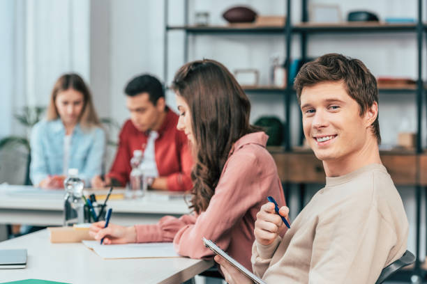 istock Happy student holding notebook with pen and looking at camera with smile 1166254754