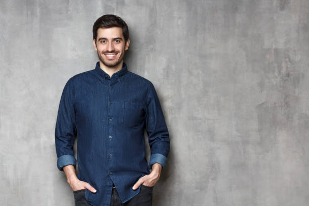 istock Young smiling man satisfied with his life standing against gray wall with copy space on the right side 1166255929