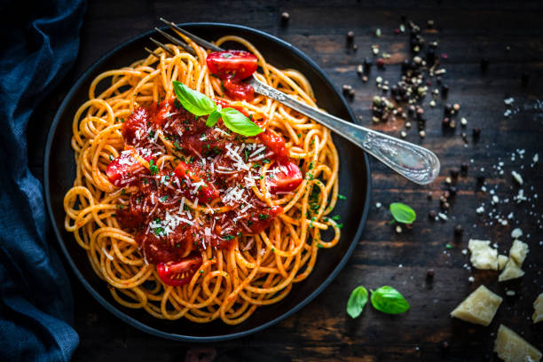 Spaghetti with tomato sauce shot on rustic wooden table Top view of spaghetti with tomato sauce plate shot on rustic wooden table. A vintage fork is inside the plate. Predominant color is red. Low key XXXL 42Mp studio photo taken with SONY A7rII and Sony FE 90mm f2.8 Macro G OSS lens italian food photos stock pictures, royalty-free photos & images