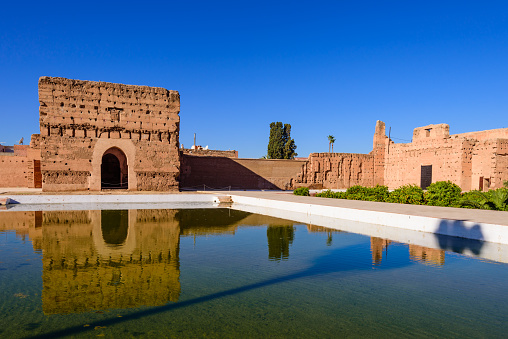 Marrakech, Morocco - December 9, 2018: Sightseeing of Morocco. El Badi Palace in Marrakech medina with reflection in water pond. A popular architectural and tourist attraction.