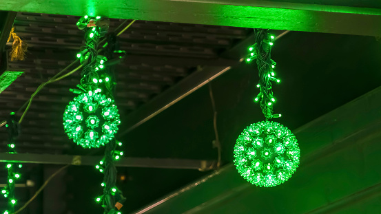 Panorama frame Close up view of several glowing neon green light balls at night. The bright and decorative light balls are hanging on the ceiling of a building.
