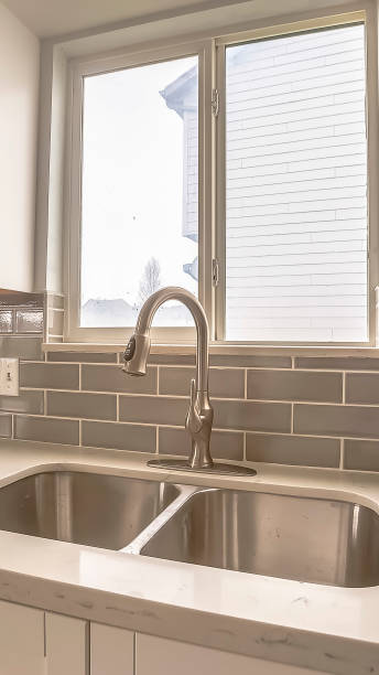 istock Vertical Double bowl stainless steel sink against tiled wall with window and cabinets 1166264593