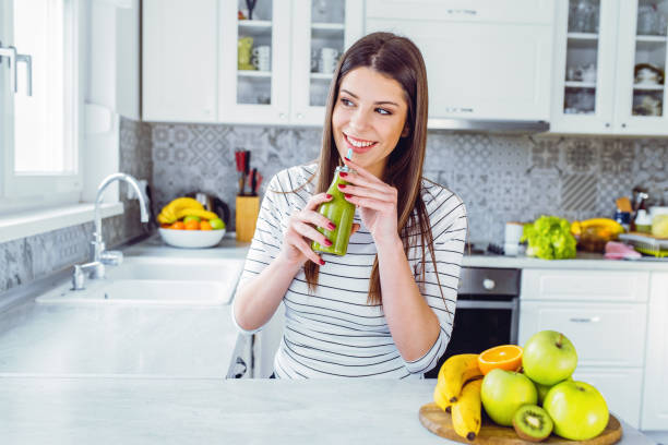 feliz adolescente beber batido sobre un fondo de color sólido - apple women green eating fotografías e imágenes de stock