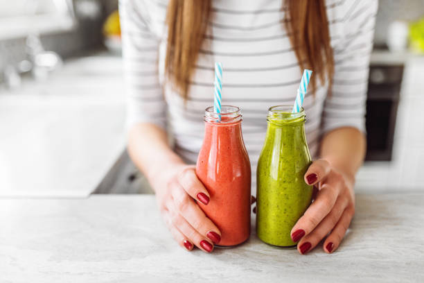 Young woman holding bottles with healthy fruit smoothies and fresh fruits. Modern white kitchen. stock photo