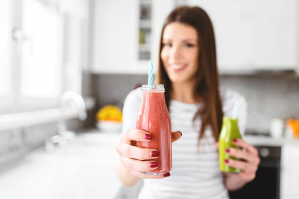 Close up of beautiful woman holding and offering red smoothie in jar. stock photo