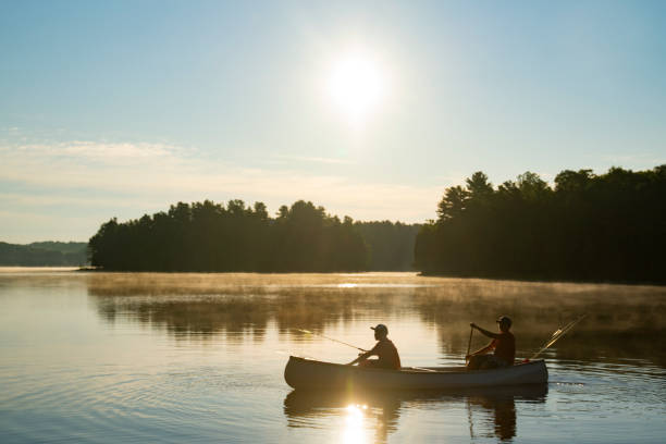 Two young fisherman in a canoe heading out onto the lake in beautiful morning light. stock photo