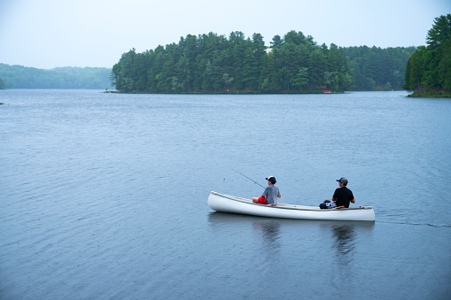 Two boys out fishing in the rain in a canoe on a lake.