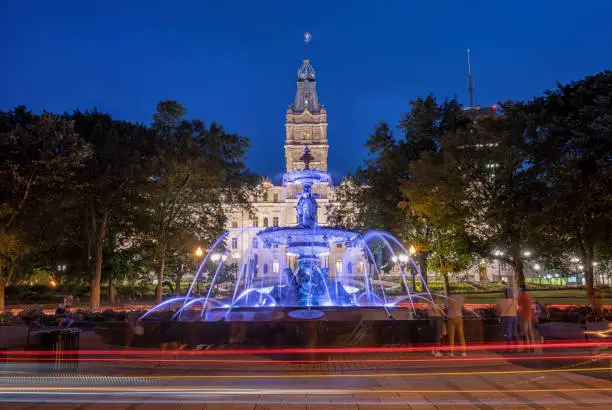A night shot of the blue fountain. The National Assembly of Quebec is in background. The Parliament Building features the Second Empire architectural style.