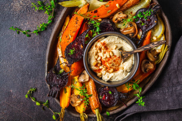 Baked vegetables with hummus in a dark dish, top view. Baked carrots, beets, zucchini and yam with hummus in a dark dish. veganism stock pictures, royalty-free photos & images