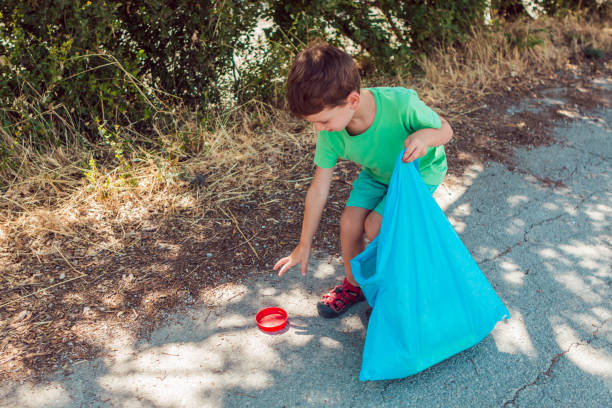 istock Little boy collecting garbage on the park while holding a blue plastic bag 1166290368