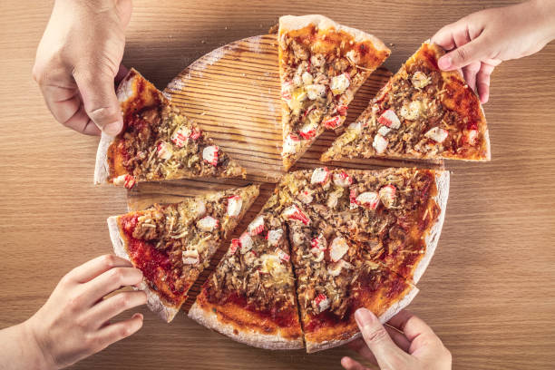 Top view of several hands of adults and children from a family taking slices of pizza stock photo