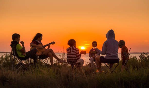people sitting on the beach with campfire at sunset Group of people sitting on the beach with campfire at sunset family bbq beach stock pictures, royalty-free photos & images