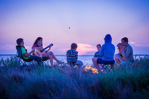 Group of people sitting on the beach with campfire at sunset