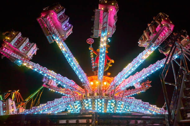 bambini che guardano un'attrazione fieristica al tramonto. persone che si godono le attrazioni del campo fieristico. - ferris wheel wheel night neon light foto e immagini stock