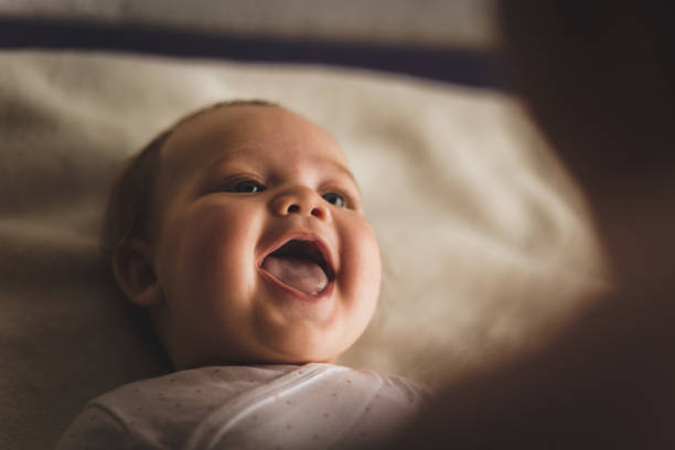 Newborn baby girl laughing and giggling while playing with her mother High angle view of cheerful newborn baby girl lying down on the bed and laughing while her mother, that is blurred in foreground, is playing with her. babyhood photos stock pictures, royalty-free photos & images