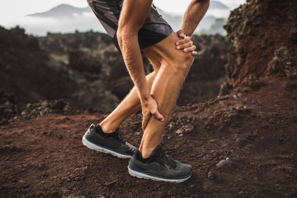 Male runner holding injured calf muscle and suffering with pain. Sprain ligament while running outdoors. Close-up legs view. stock photo