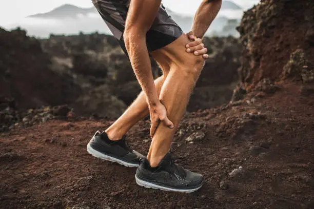 Male runner holding injured calf muscle and suffering with pain. Sprain ligament while running outdoors. Close-up legs view.