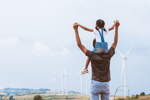 Father and daughter having fun to play together. Asian child girl riding on father's shoulders in the wind turbine field