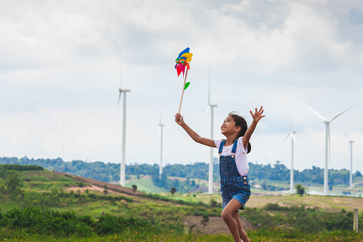 Cute asian child girl is running and playing with wind turbine toy  with fun in the wind turbine field