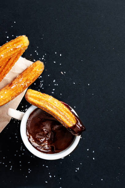 istock Churros with sugar dipped in chocolate sauce on a black background. Churro sticks. Fried dough pastry, top view 1166312343