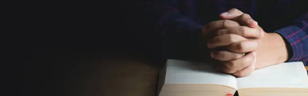 Hands of praying young man and Bible on a wooden table.