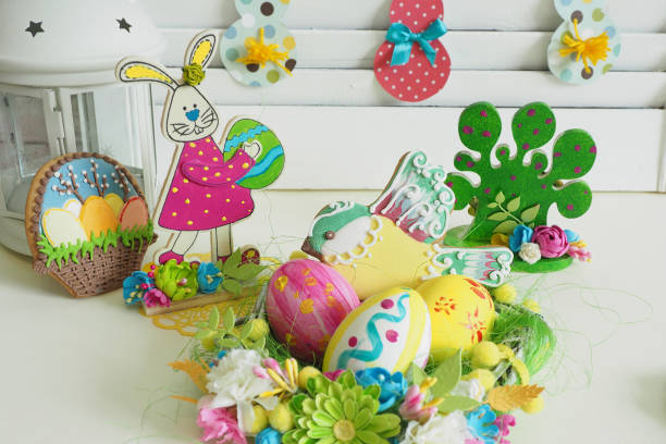 Easter home decor. paper garland with bunnies, wooden bunny figurine with eggs, hand-painted, handmade basket with eggs and gingerbread, painted by hand, wooden figure of a tree, painted by hand and decorated with handmade flowers. decoración del hogar de pascua. guirnalda de papel con conejos, figura de conejito de madera con huevos, cesta hecha a mano, con huevos y pan de jengibre, pintada a mano, figura de madera de un árbol, pintada a mano y decorada con flores hechas a mano.