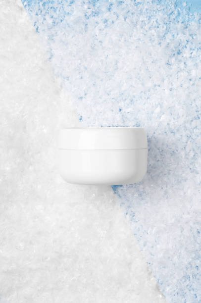 White jar with face cream on a white and blue background with artificial snow. Cosmetic moisturizing winter product. Copy space, top view, flat lay.