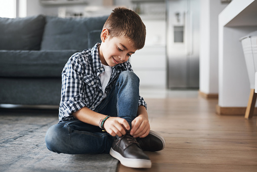 Shot of an adorable little boy tying his shoelaces at home