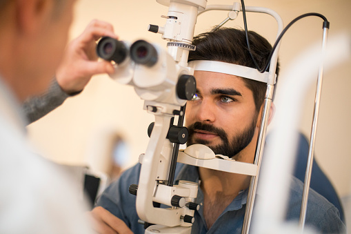 Young man during an eye exam with an optometrist. Young man is about 25 years old, optometrist is about 65 years old, both Caucasian males.