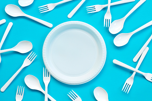 Plastic plate, forks, spoons on blue background.
