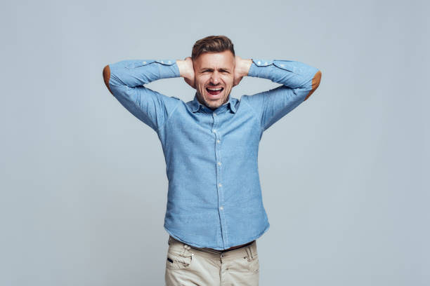 Bla bla bla. Depressed man closing ears with both hands and screaming while standing against grey background Bla bla bla. Depressed man closing ears with both hands and screaming while standing against grey background. Stress emotion. Noise concept man closing ears photos stock pictures, royalty-free photos & images
