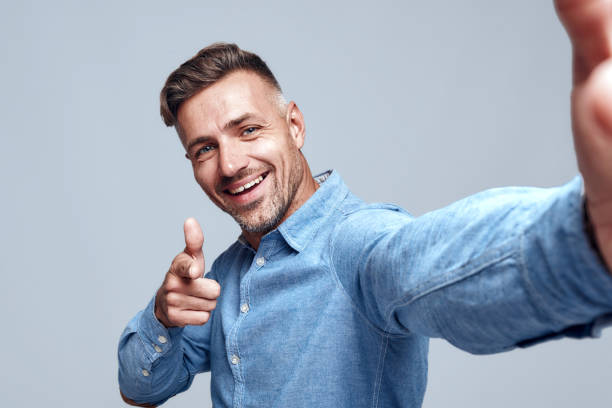 istock Keep smiling! Cheerful bearded man in shirt making selfie and gesturing while standing against grey background. 1166342974