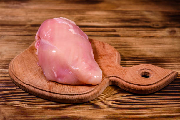 istock Cutting board with raw chicken fillet on wooden table 1166344021