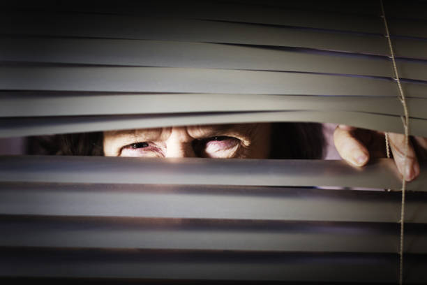 istock Senior woman squints through venetian blind, having difficulty seeing 1166345279